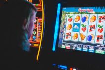 A person with long hair stares at the flat screen of an electronic gambling machine. Fruit, bells and other colourful icons are in columns on the screen.