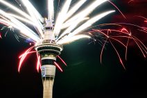 Sky Tower, by the casino in Auckland, has fireworks spurting out of its top in all directions. The sky is dark and some of the fireworks look neon-coloured.