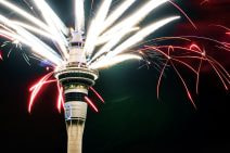 Sky Tower, by the casino in Auckland, has fireworks spurting out of its top in all directions. The sky is dark and some of the fireworks look neon-coloured.