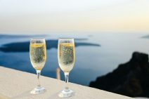 Two glasses of bubbling champagne sit on white stone, overlooking the ocean.