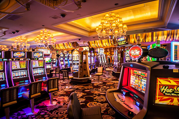 An electronic gaming machine lounge is set in golden tones. The area has a subtle feeling of luxury with its elaborate chandeliers and decorative ceilings. 