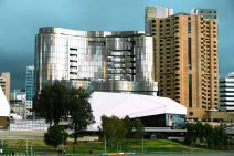 SkyCity Adelaide’s shiny silver and curved building is sitting next a large taller brown building. A blue and grey sky is clear behind them.